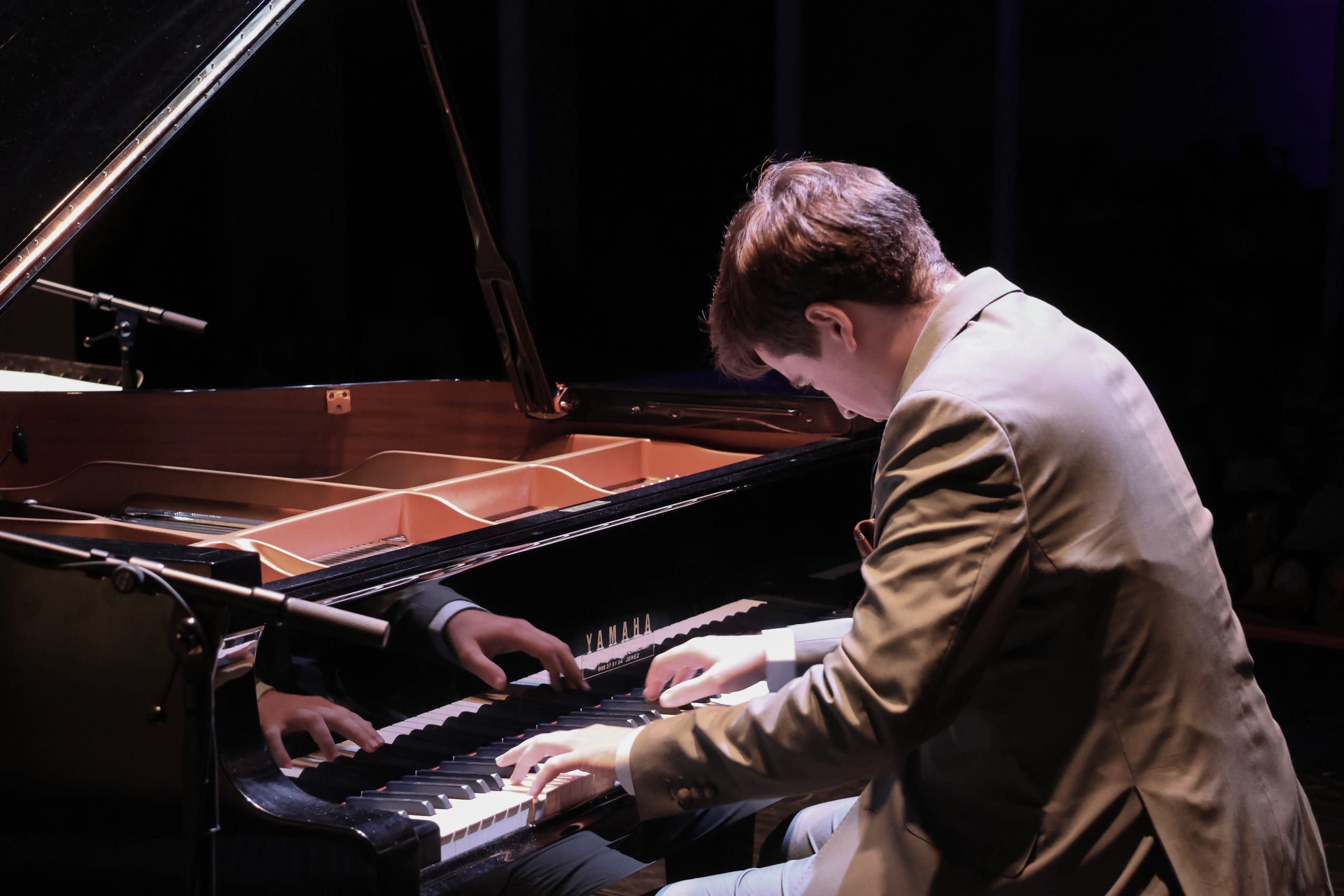Javier Cecilia tocando un piano de cola abierto, iluminado por luz cálida de teatro